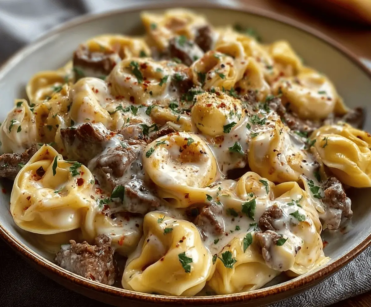 Creamy cheesesteak tortellini topped with melted provolone cheese served in a savory sauce, garnished with fresh herbs