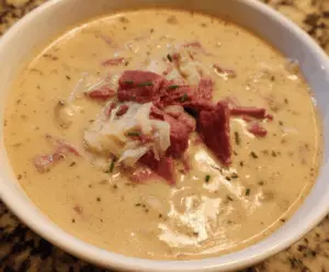 Creamy Reuben Soup in a bowl topped with melted cheese, corned beef, sauerkraut, and fresh herbs, served with crusty bread