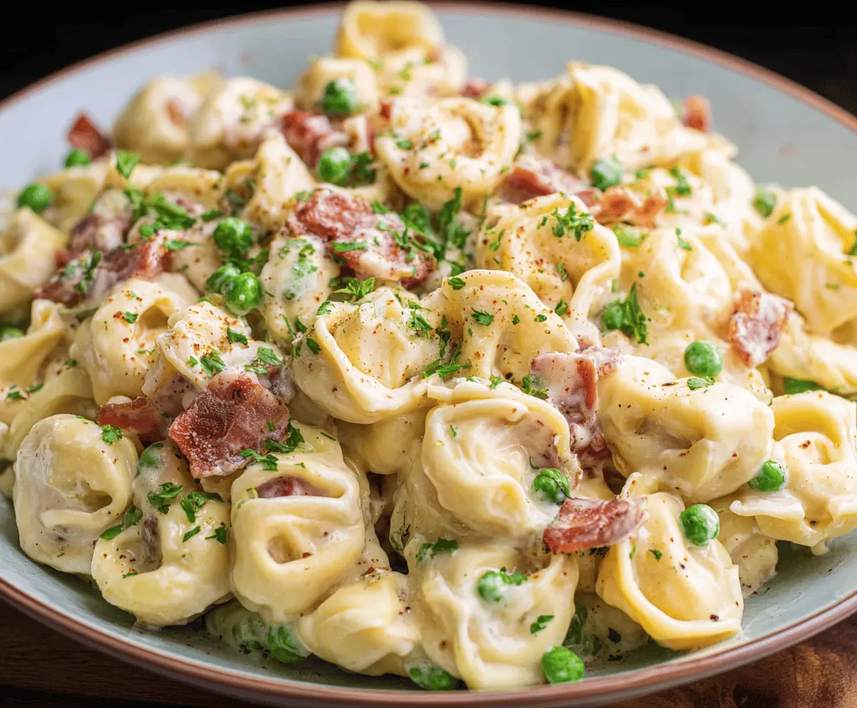 Creamy tortellini carbonara served in a white bowl, garnished with fresh herbs and grated Parmesan cheese, featuring a rich, creamy sauce and crispy bacon bits.