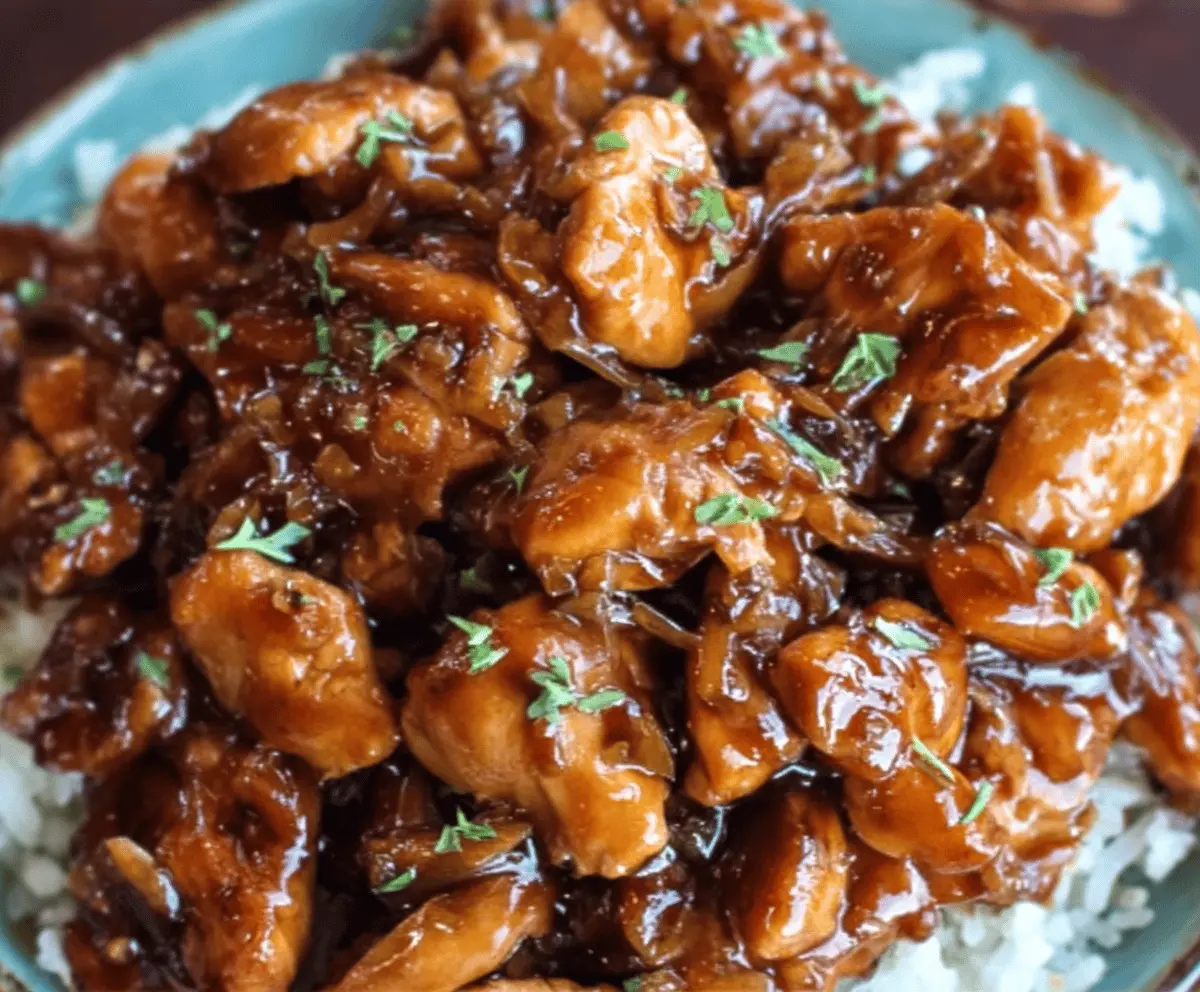 Delicious Crock Pot Bourbon Chicken served over rice with a glossy glaze and garnished with green onions