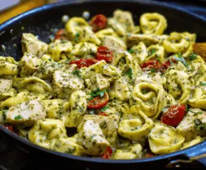Delicious pesto chicken tortellini dish with fresh basil, creamy pesto sauce, grilled chicken pieces, and melted cheese, served on a white plate