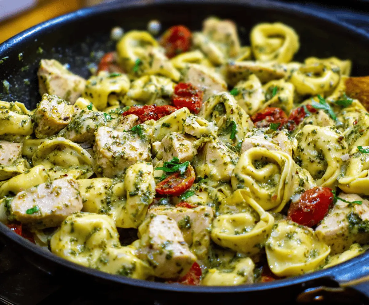 Delicious pesto chicken tortellini dish with fresh basil, creamy pesto sauce, grilled chicken pieces, and melted cheese, served on a white plate