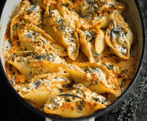 Delicious vegan pumpkin ricotta stuffed shells garnished with fresh herbs on a white plate, perfect for a cozy fall meal.