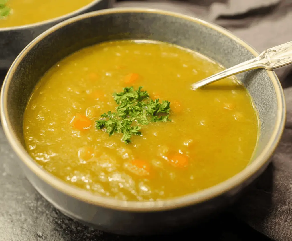 A bowl of creamy split pea soup garnished with fresh herbs and served with crusty bread on a rustic wooden table.