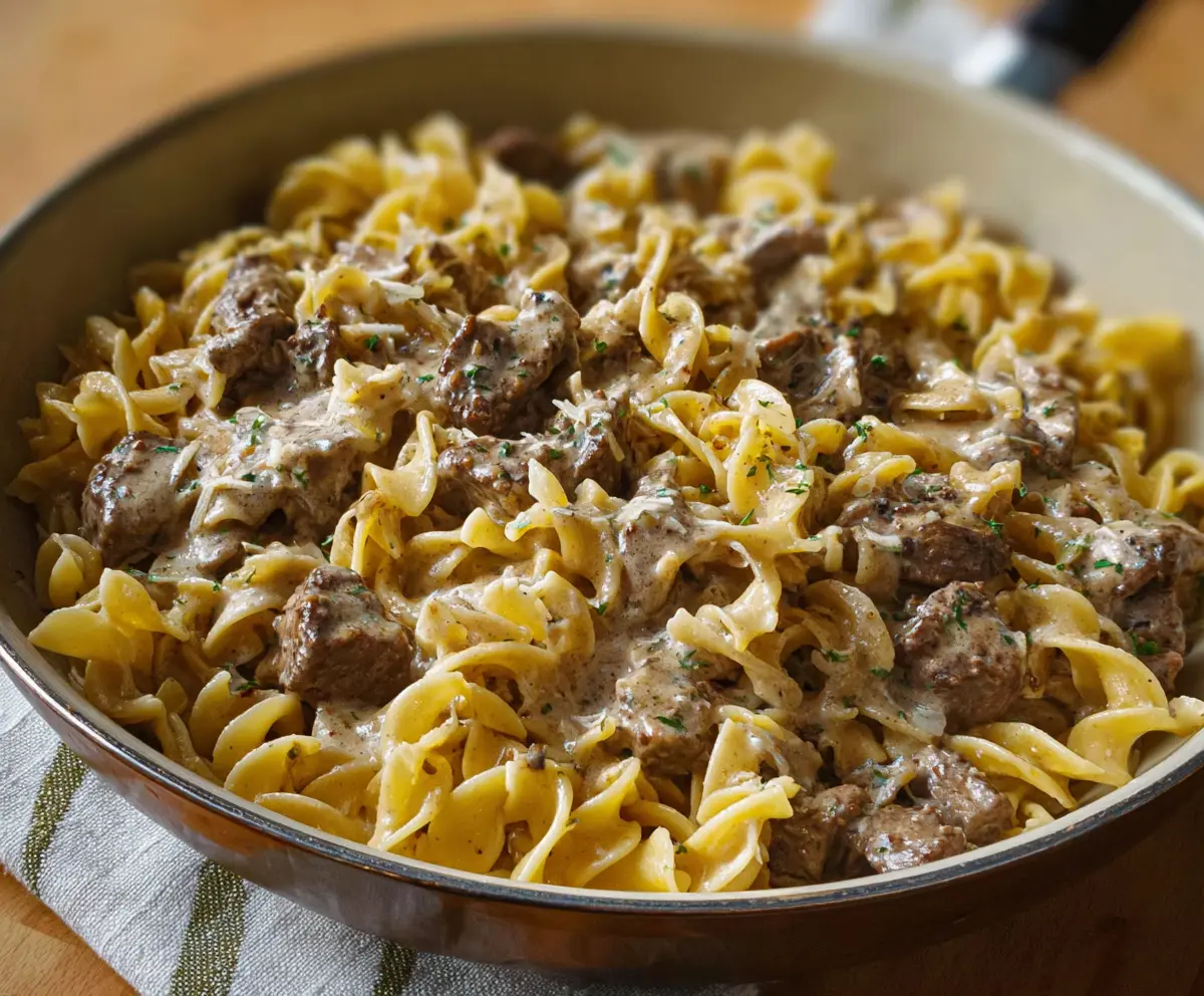 Creamy beef stroganoff served over noodles in a white bowl with parsley garnish