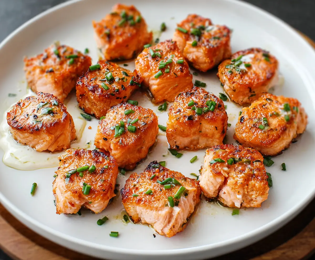 Delicious and juicy salmon bites served on a white plate, garnished with fresh herbs.