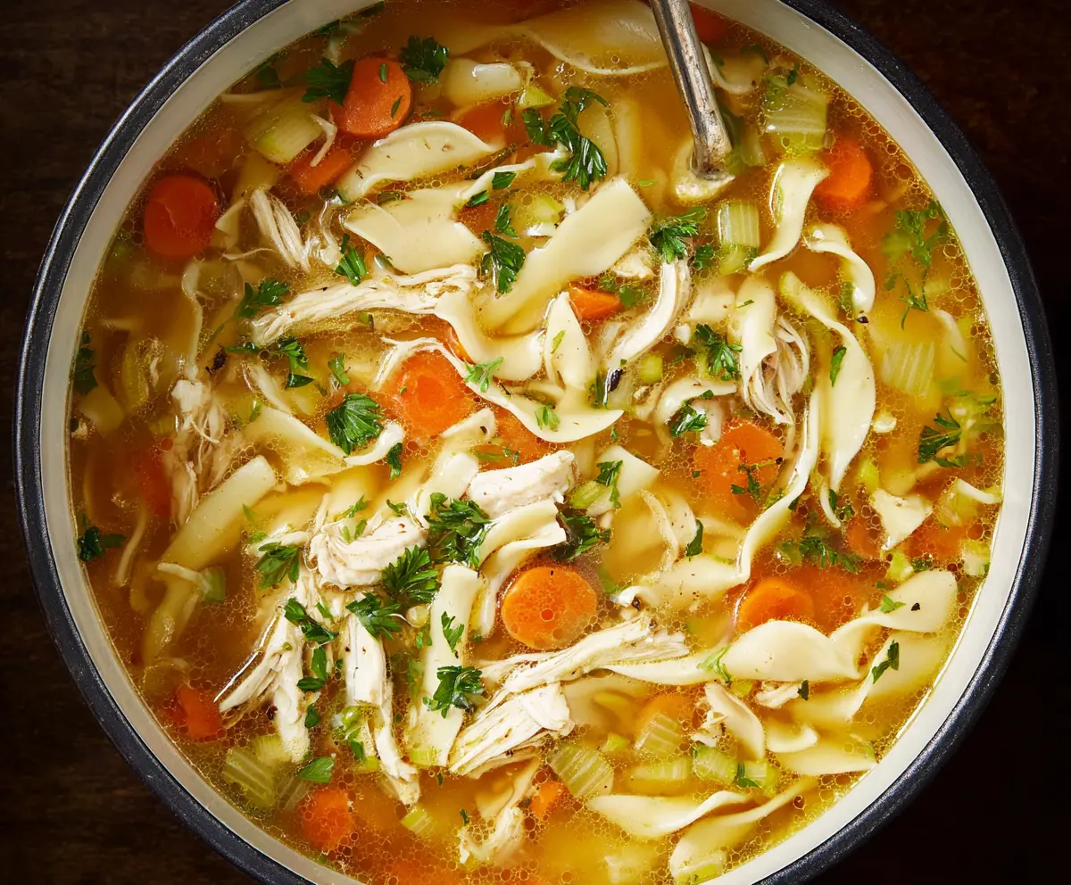 Warm and comforting traditional chicken noodle soup in a bowl, topped with fresh herbs