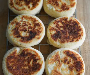 Homemade sourdough discard English muffins on a wooden cutting board with butter and jam